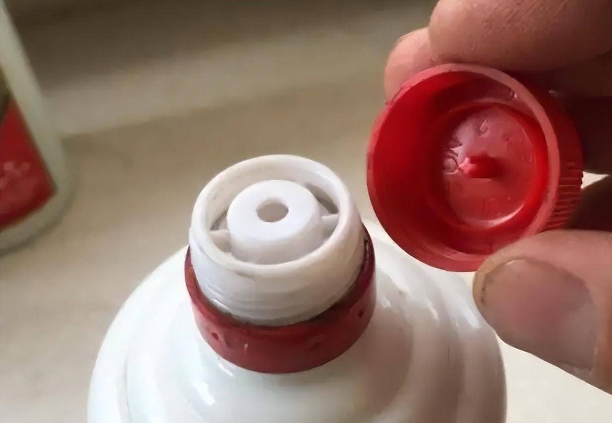 A red screw cap held beside the white self-sealing pourer of an opened bottle, photographed close up