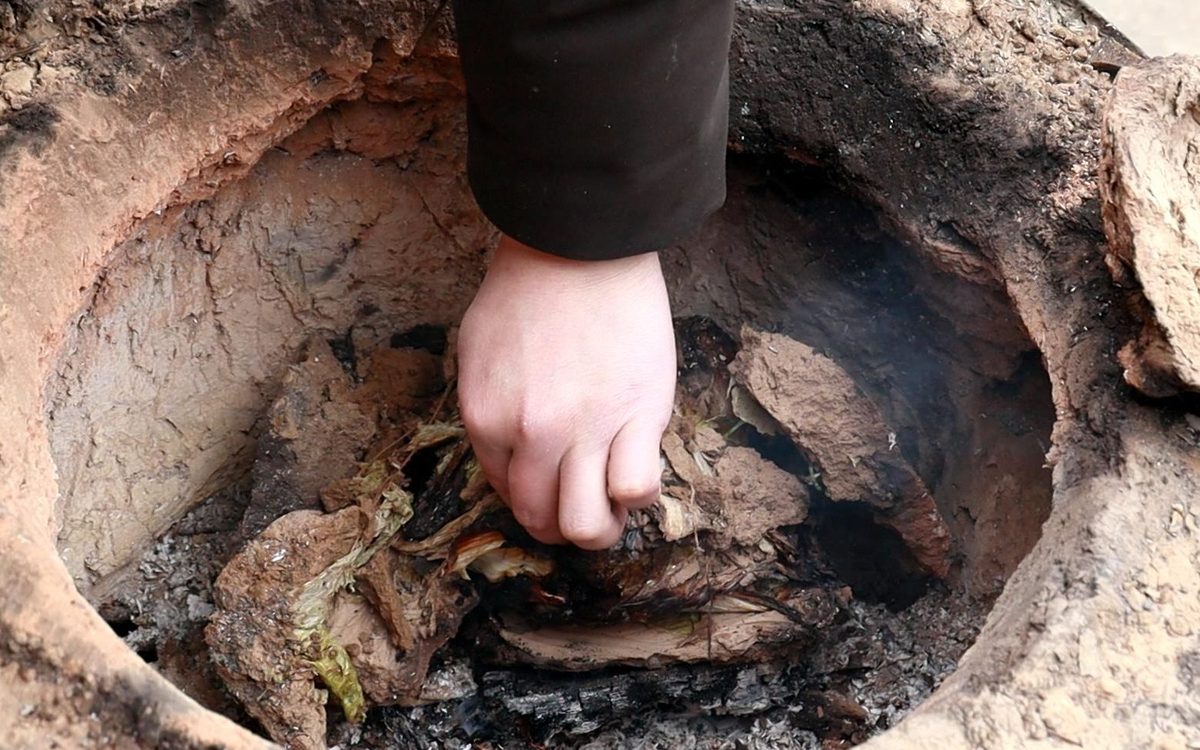 Beggar's Chicken — the mud-sealed package being pulled from an earthen pit of ash and embers