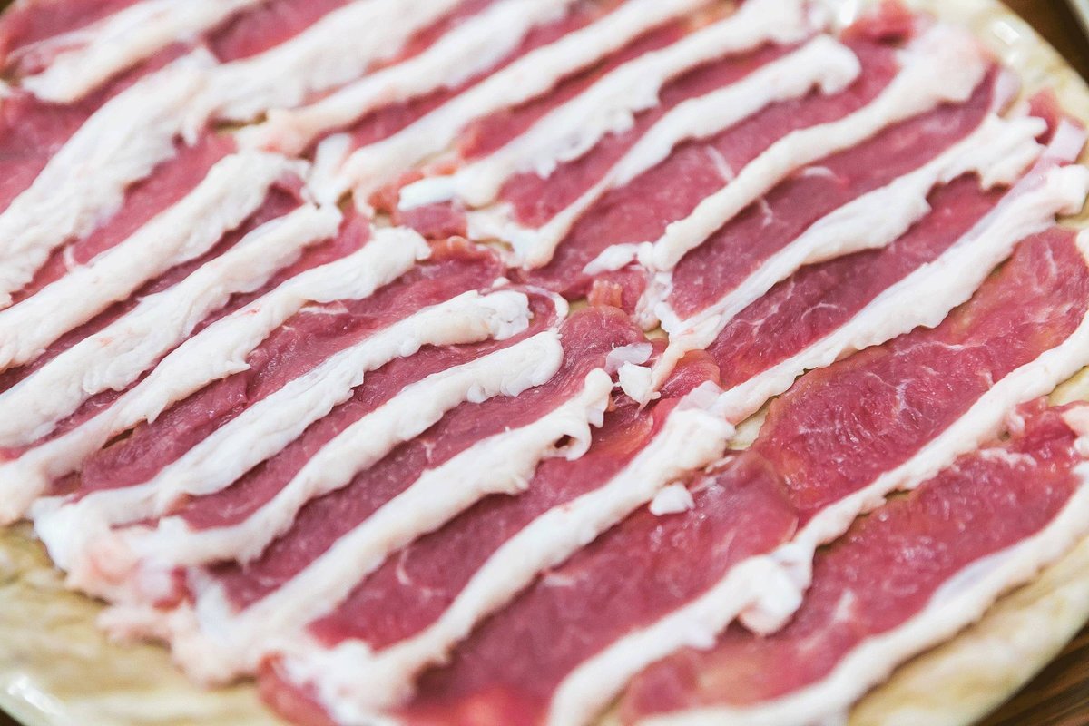 Hand-cut lamb for hot pot — overlapping slices of deep red meat with thick white fat bands, fanned out across a plate