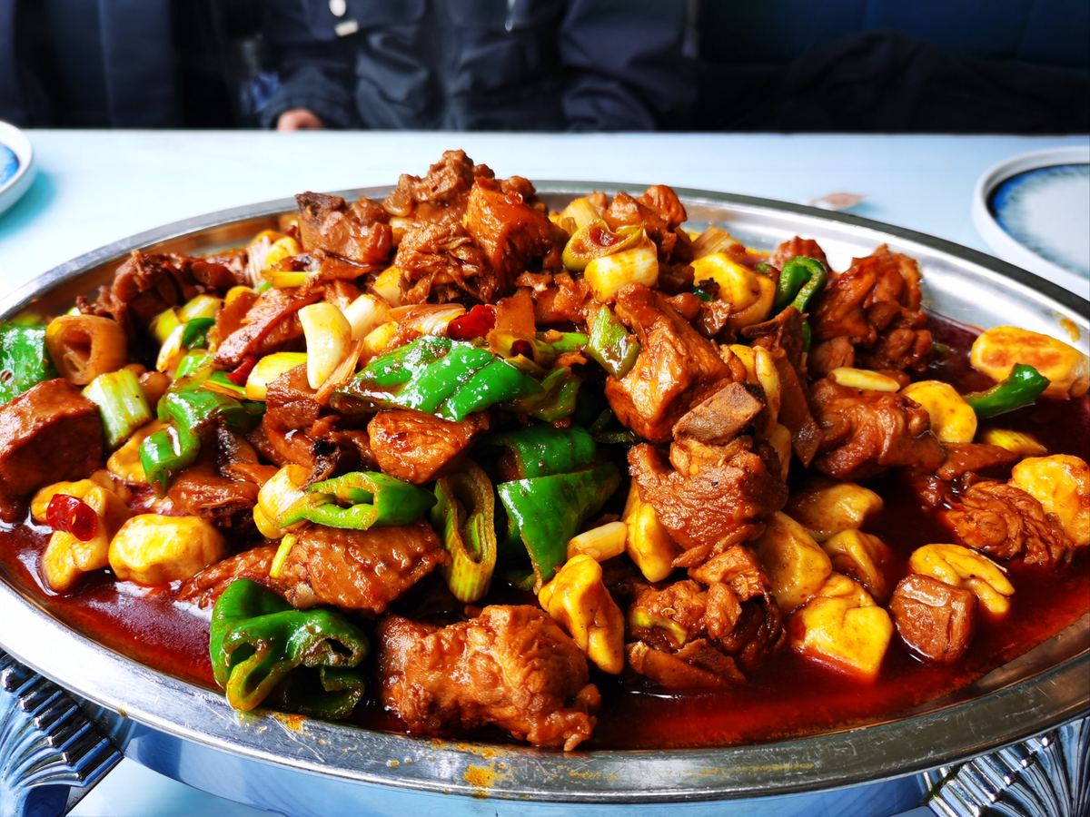 Big-Plate Chicken — glossy chicken pieces and floury potato wedges in chili-red sauce, close up in a steel platter