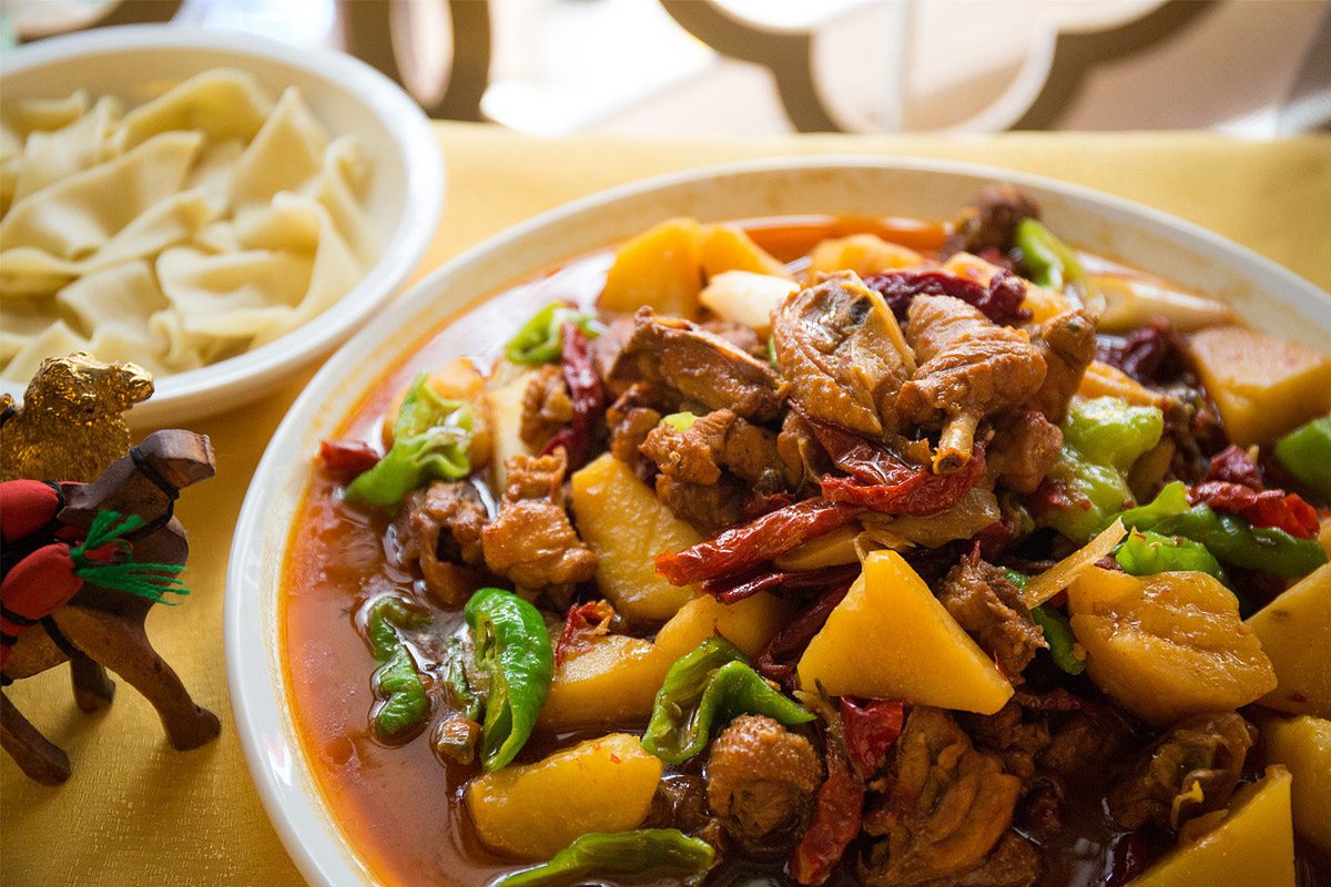 Big-Plate Chicken on a restaurant table with a bowl of wide hand-pulled belt noodles beside it