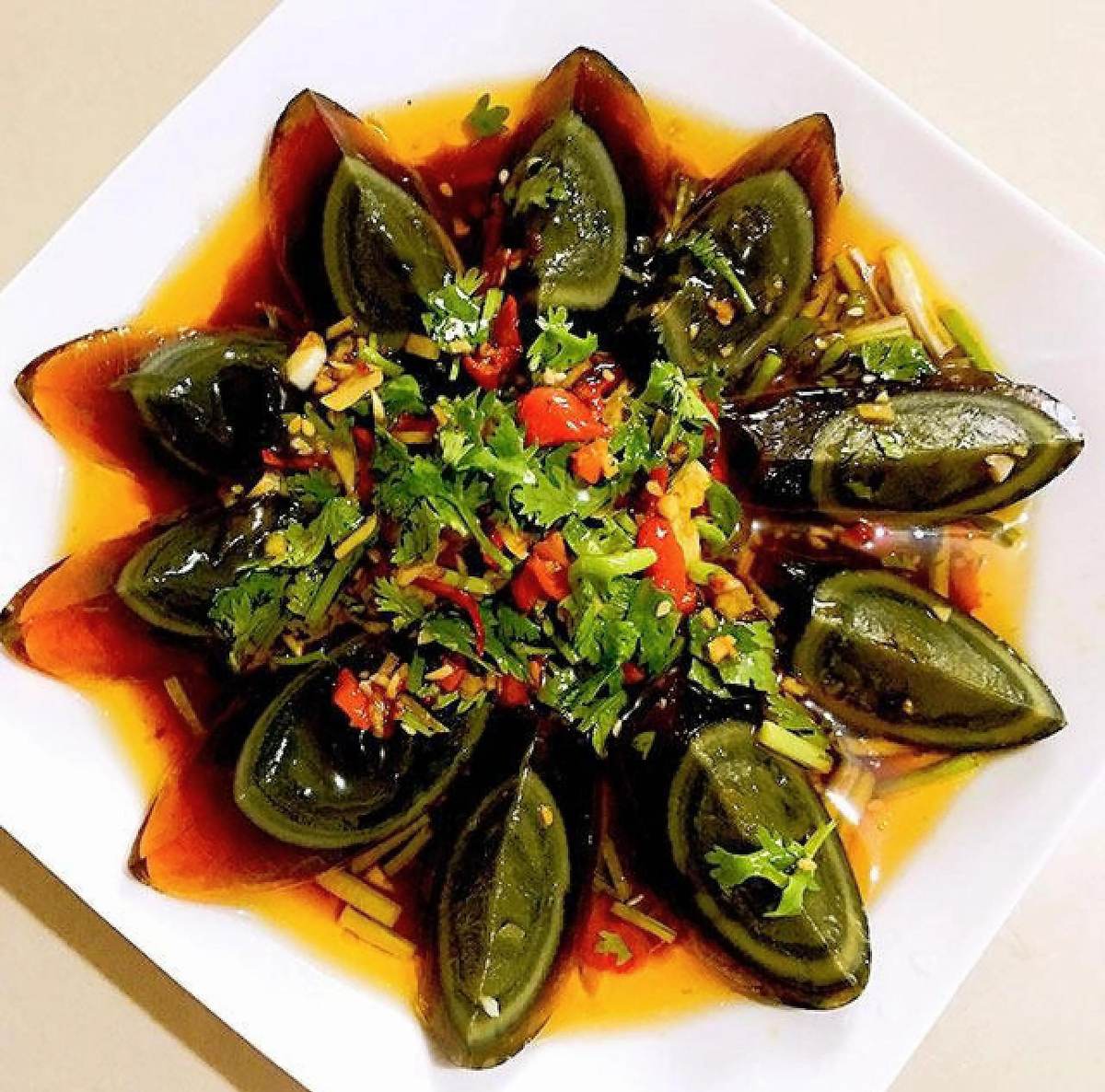 Century Egg — wedges fanned around a plate, amber jelly white against the dark yolk, chilli and garlic on top
