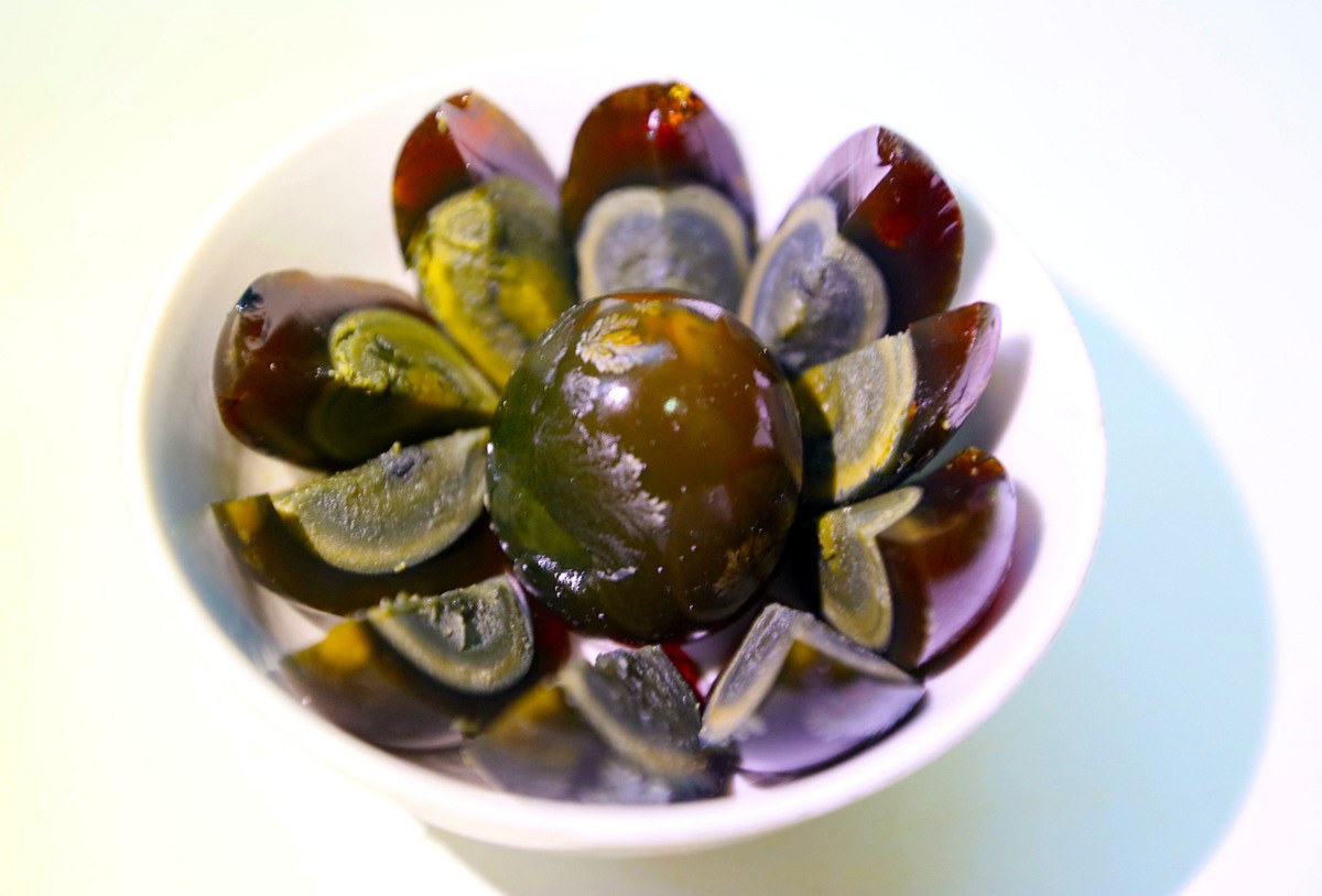 Century egg close-up — one whole egg ringed by cut wedges, the translucent amber white and green-black yolk