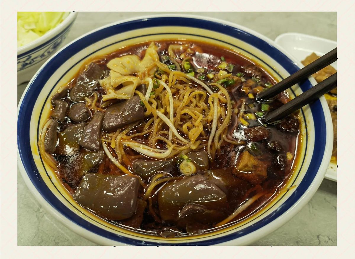 A bowl of changwang mian served at a restaurant table with chopsticks, pickled vegetables and side dishes — the way it arrives in a Guiyang noodle shop