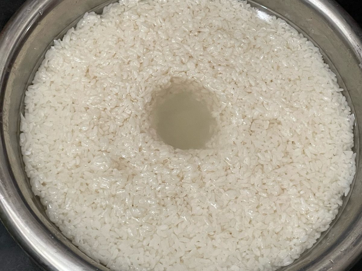 Glutinous rice left to ferment in a steel bowl, a well pressed into the centre to catch the sweet liquid