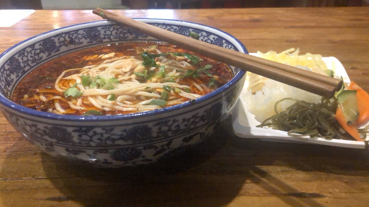 Chongqing Xiaomian served on a wooden table with chopsticks and a side plate
