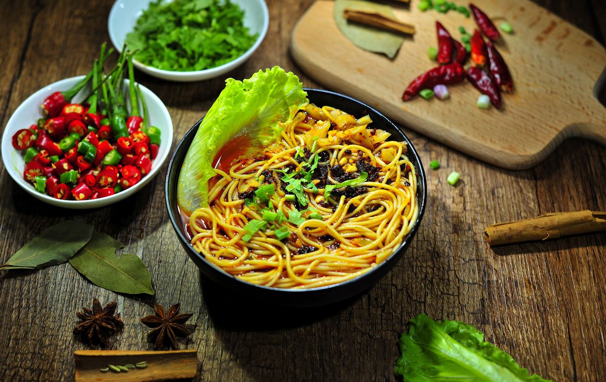 Chongqing Xiaomian close-up — noodles lifting out of glossy red chili oil with scallion and fresh chilli