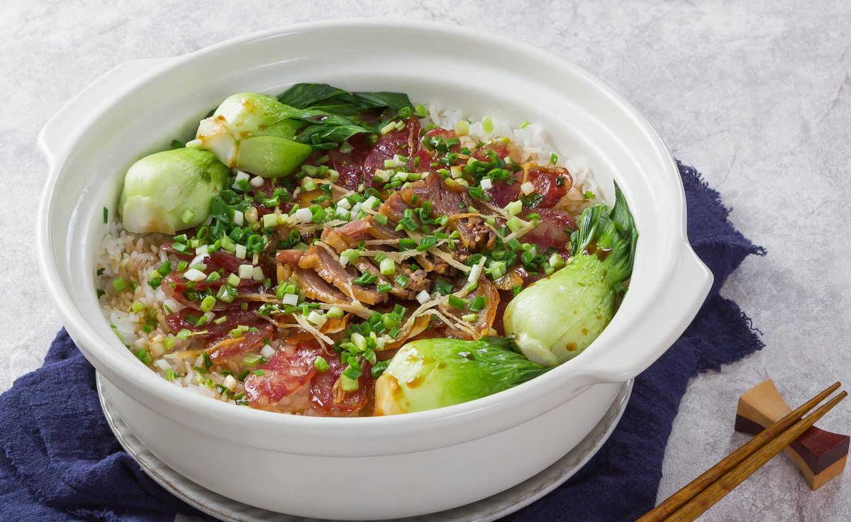 Claypot Rice served at the table with a bowl of broth, soy sauce and a plate of greens
