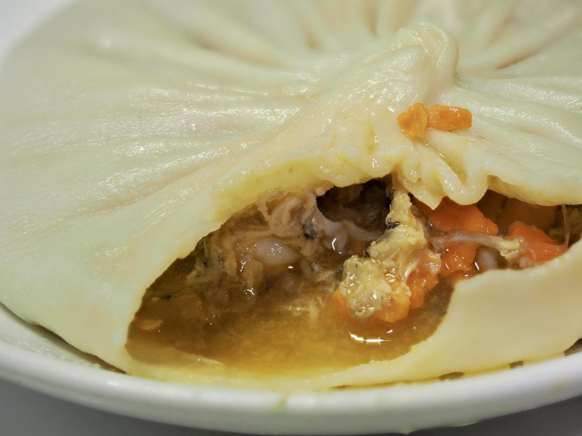 Crab Roe Soup Dumpling — torn open, releasing amber broth and the orange crumb of crab roe