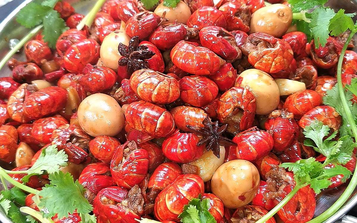 Crayfish tails close-up — the prize, glossy with chilli oil, star anise and quail eggs in the pan