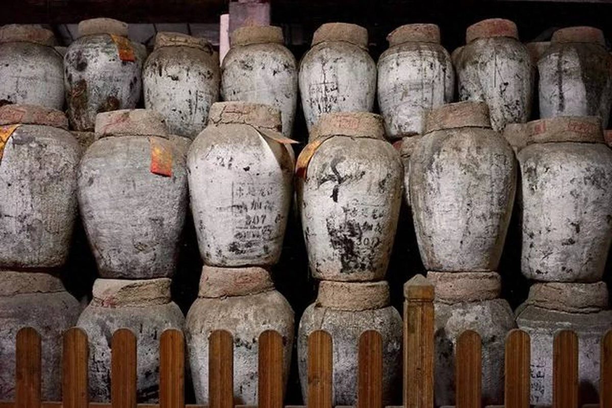Stacked huangjiu jars marked with painted batch numbers behind a wooden rail