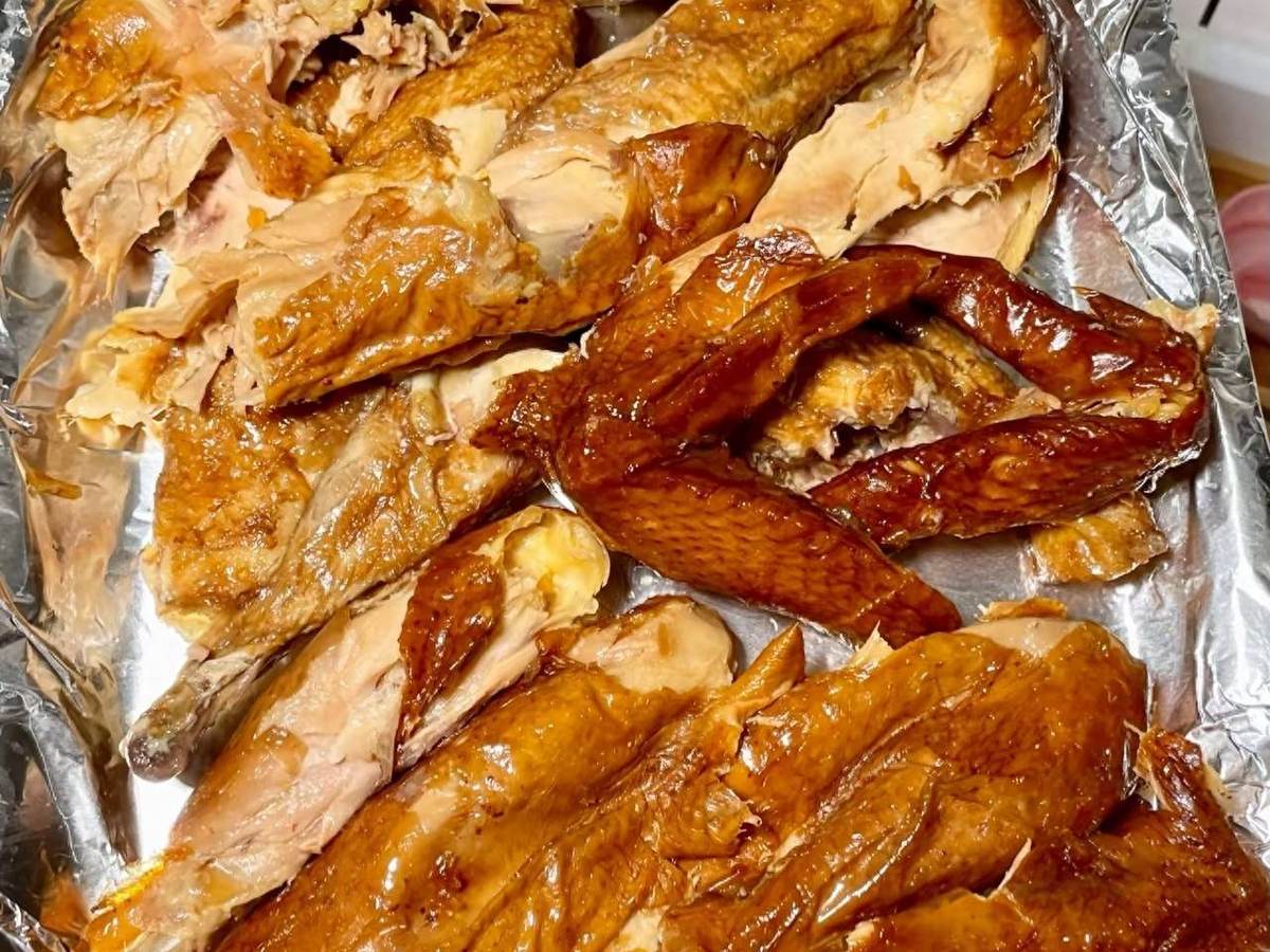 Dezhou braised chicken close-up — hand-torn pieces with golden skin and pale meat pulling away from the bone on crumpled paper