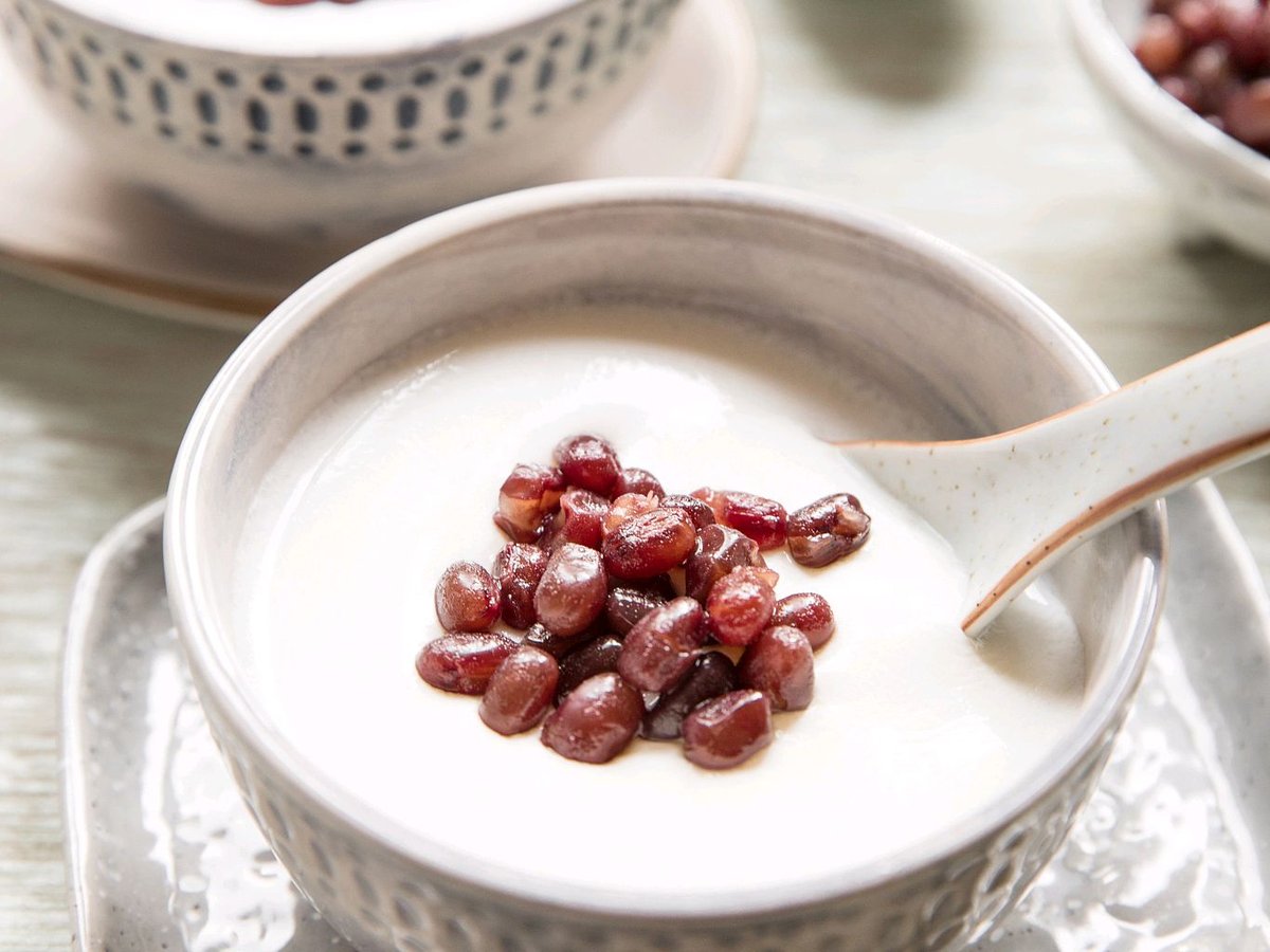 Double-skin milk topped with sweet red beans, a spoon resting in the custard, more bowls blurred behind it