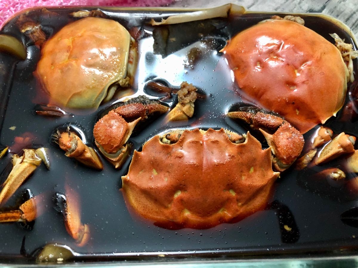Crab shells, claws and legs steeping in a tray of almost-black marinade on a kitchen counter, the cure partway through