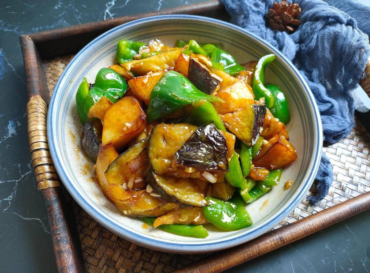 Earth's Three Fresh — a close-up of sauce-coated eggplant, potato and green pepper in a blue-rimmed bowl