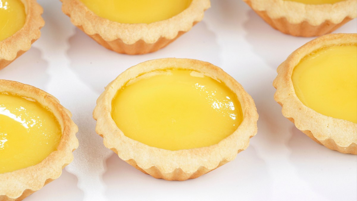 Egg tarts on a tray, custard pale and glassy in fluted pastry shells — the classic Hong Kong version