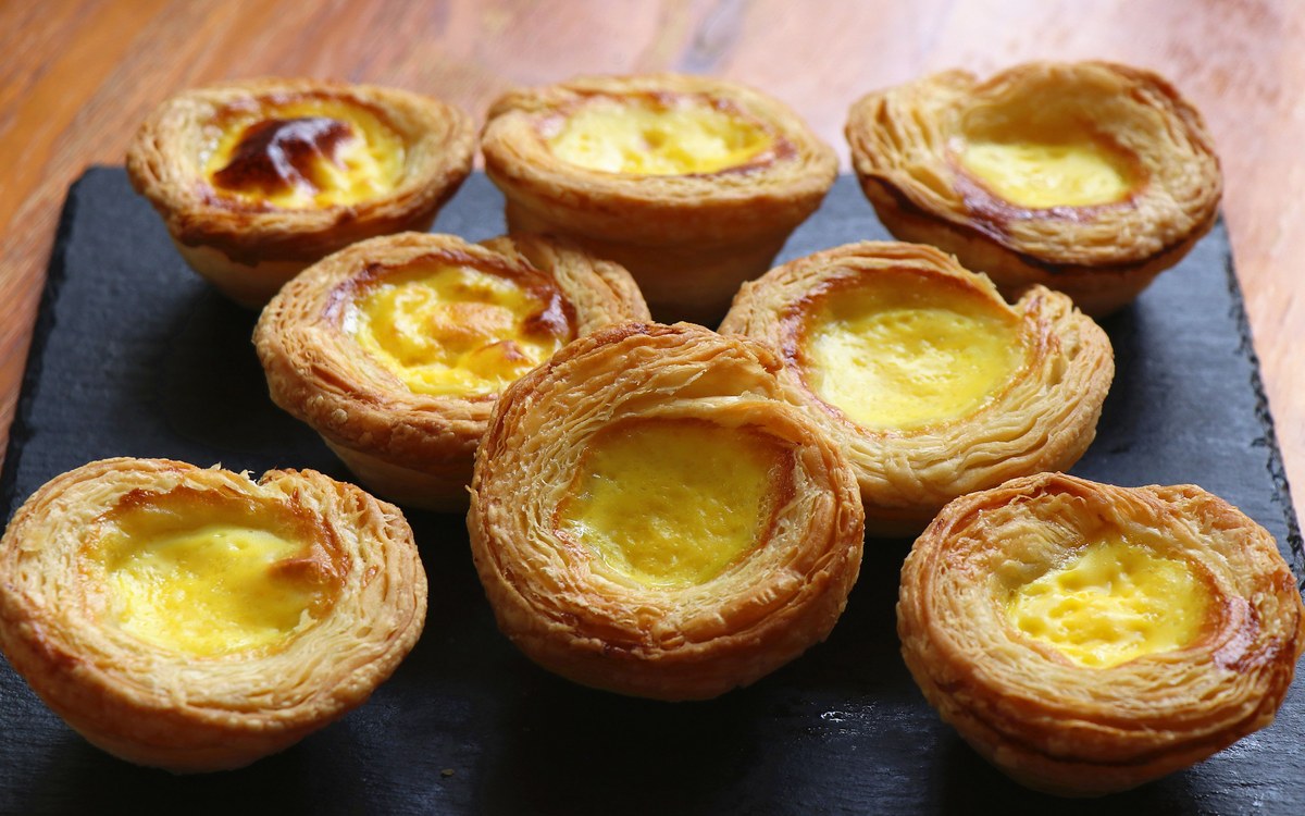 Egg tarts with blistered, caramelised tops on a slate board — the Macau-Portuguese nata style, which is a different tart