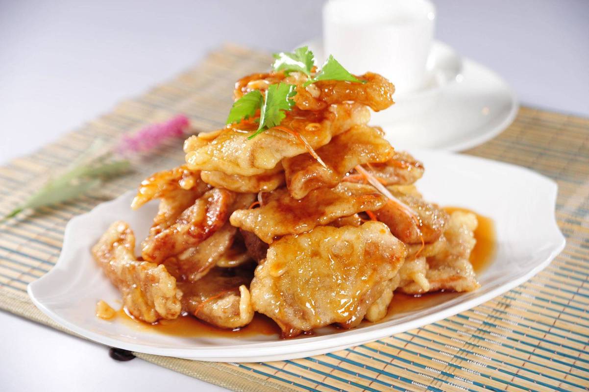 Guo Bao Rou — a generous plate of golden pork slices on a family-style table, chopsticks reaching in