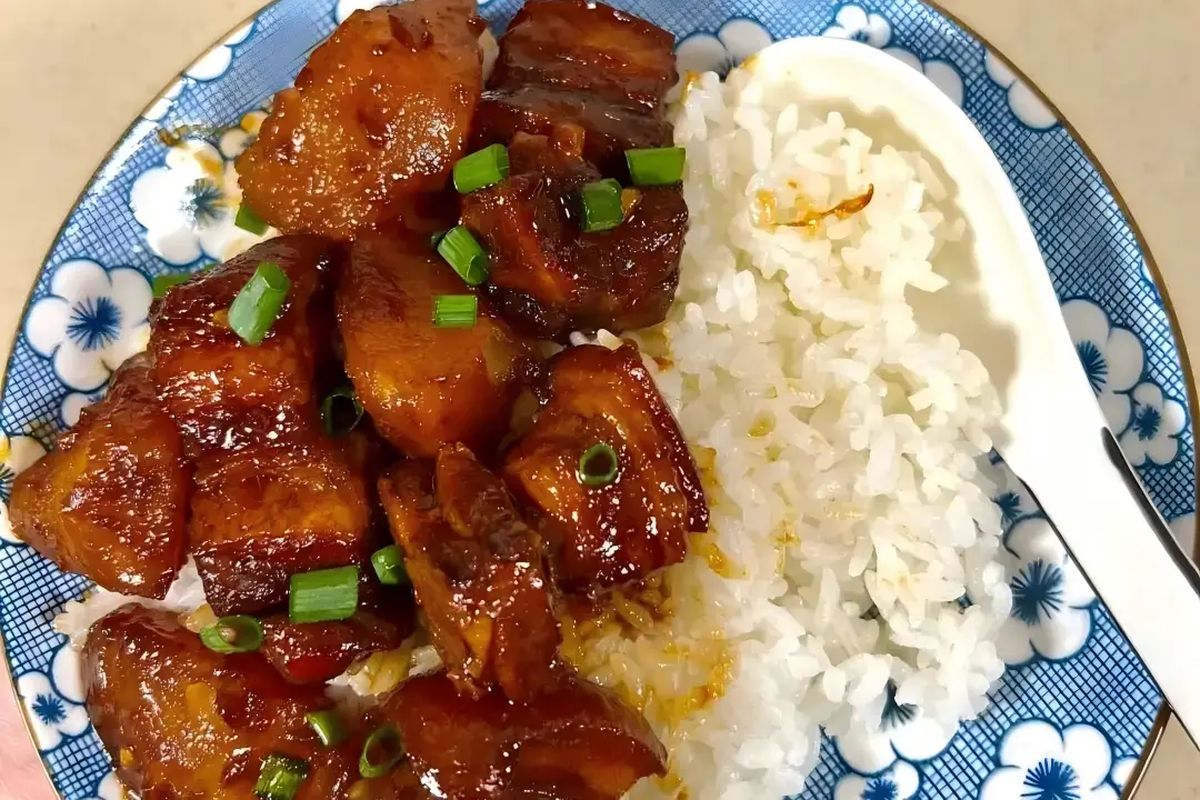 Hóngshāo ròu in a white bowl, ready to serve, chopsticks poised