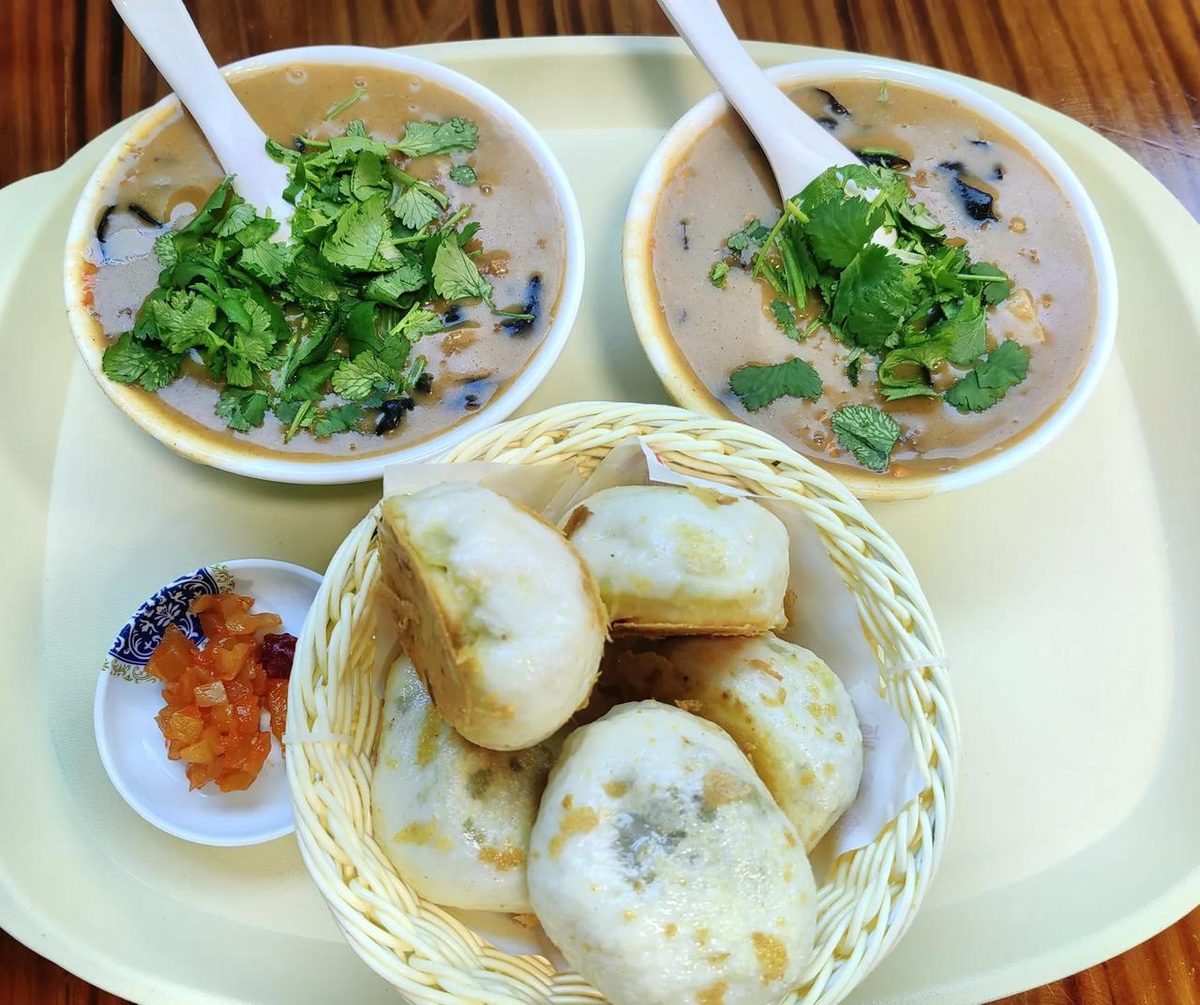 A Henan breakfast table — two bowls of Hu La Tang under a heap of coriander, beside a basket of pan-fried pork buns and a dish of pickles