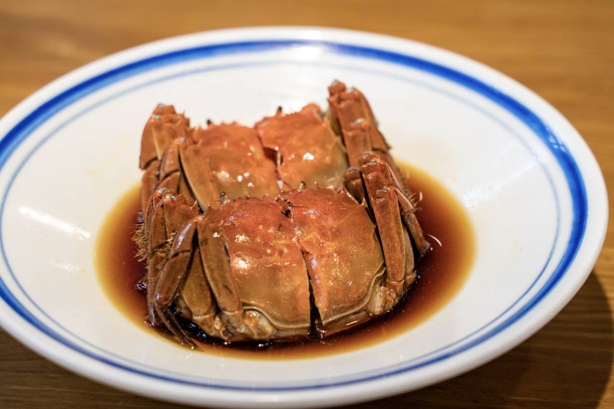 Steamed hairy crabs on a white plate with a dark dipping sauce, a wooden table behind