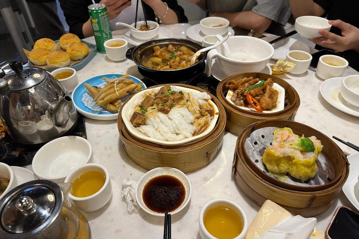 A Cantonese dim sum table crowded with bamboo steamers, rice noodle rolls and teapots