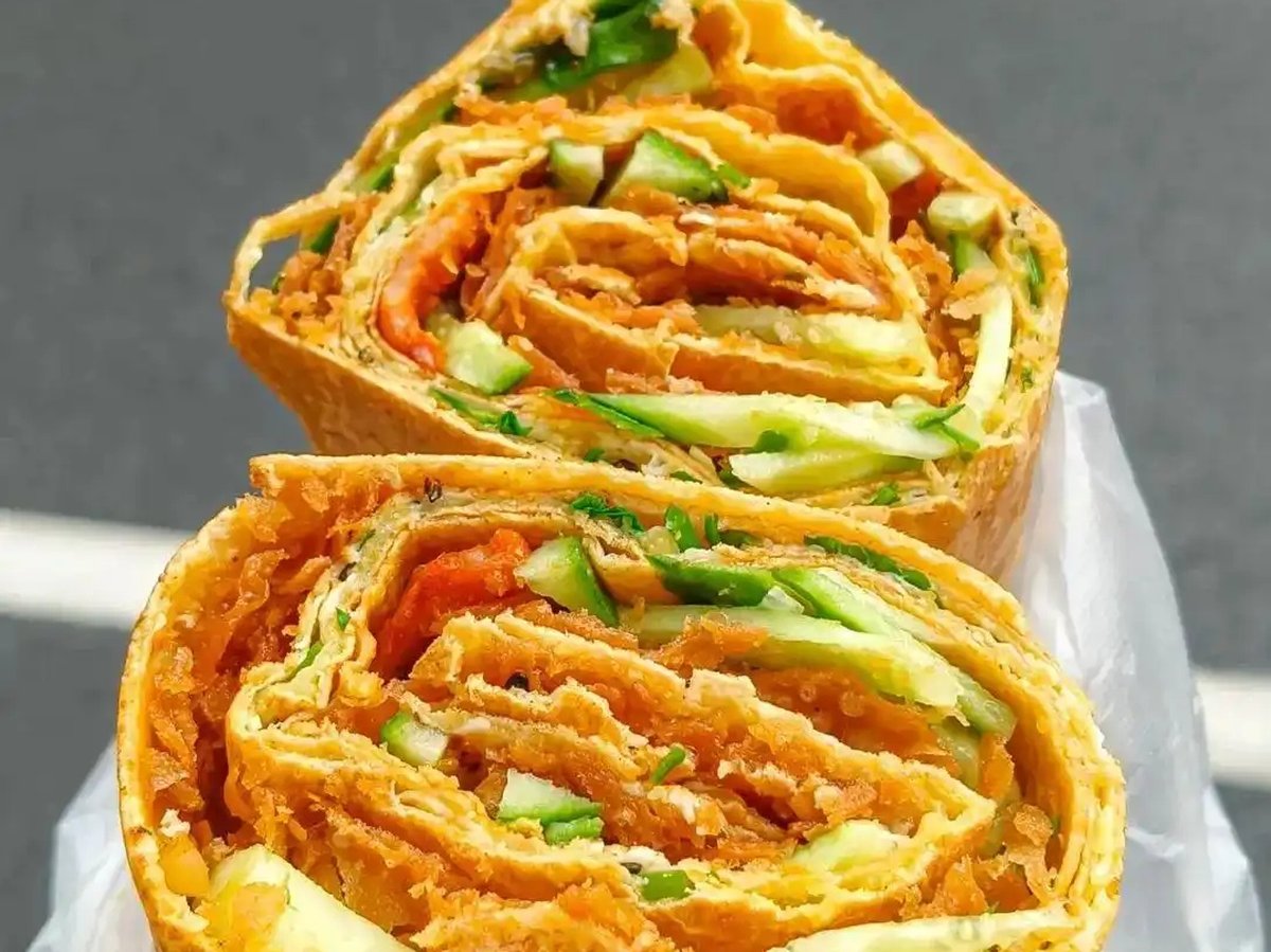 Jianbing — finished crepe folded in hand, brown paper wrapper, steam rising, morning light