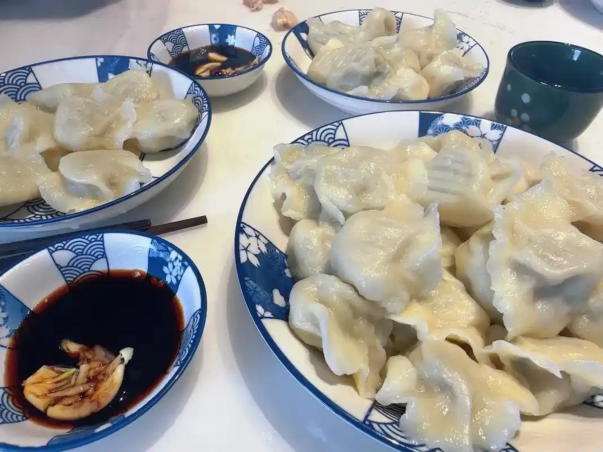 Jiaozi on a plate — boiled dumplings glistening, a small dish of black vinegar with ginger shreds on the side, chopsticks reaching in