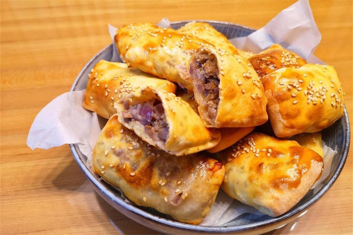 Kao baozi — a metal bowl of square baked lamb buns lined with paper, one torn open to show diced lamb and sweet onion