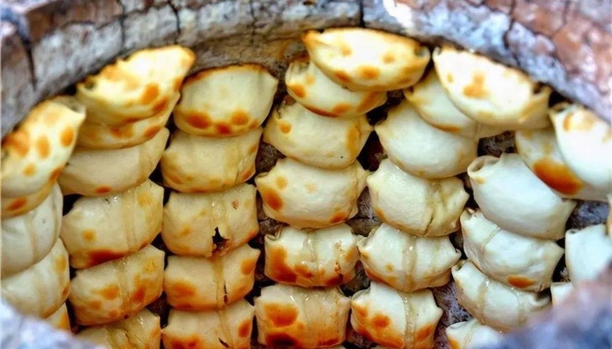 Kao baozi baking on the clay wall — square folded parcels with blistered, scorched faces where the dough meets the heat