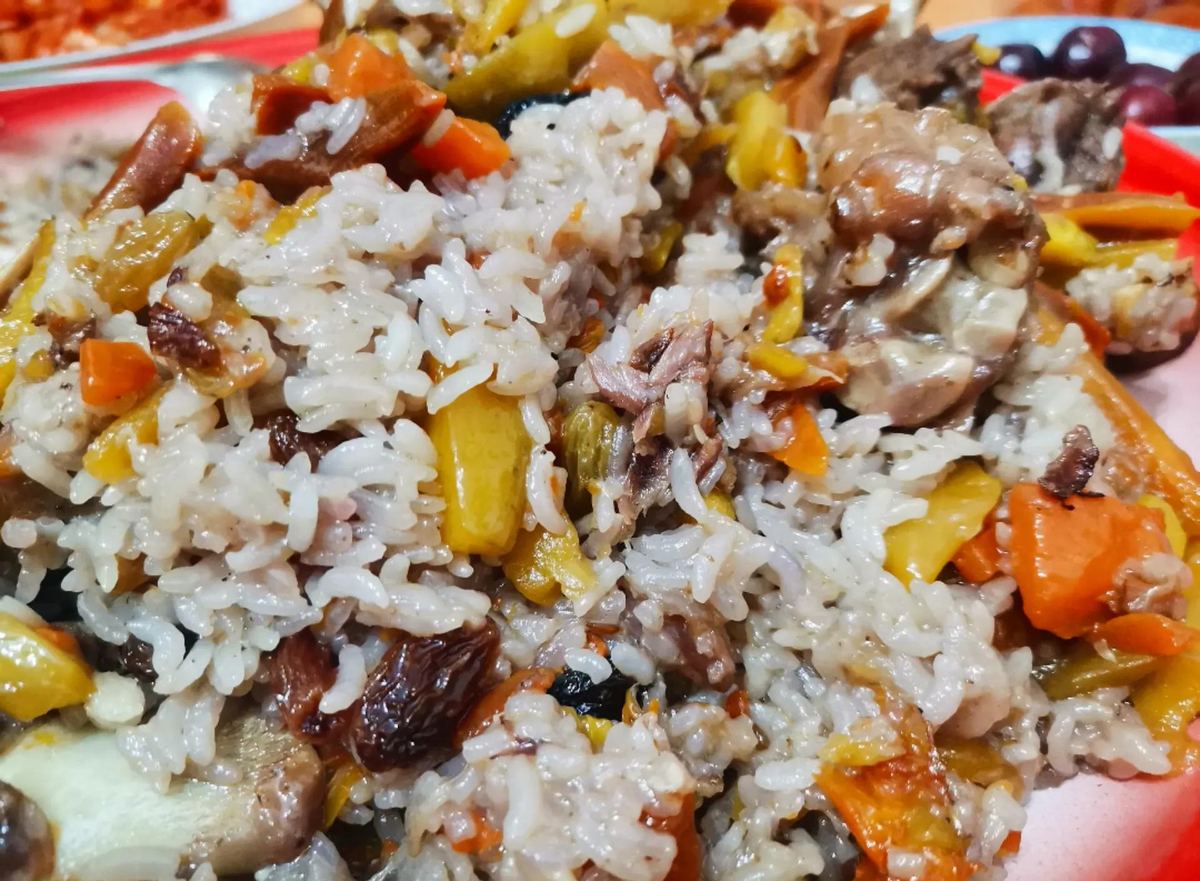 Lamb pilaf close-up — separate grains of rice stained orange and yellow, julienned carrots, raisins and chunks of bone-in lamb