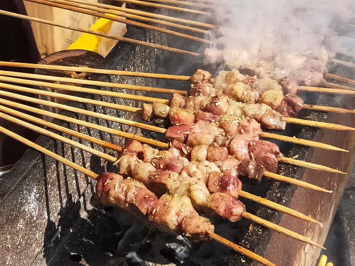 Lamb skewers on the charcoal grill — fat and lean alternating, cumin going on, smoke coming up