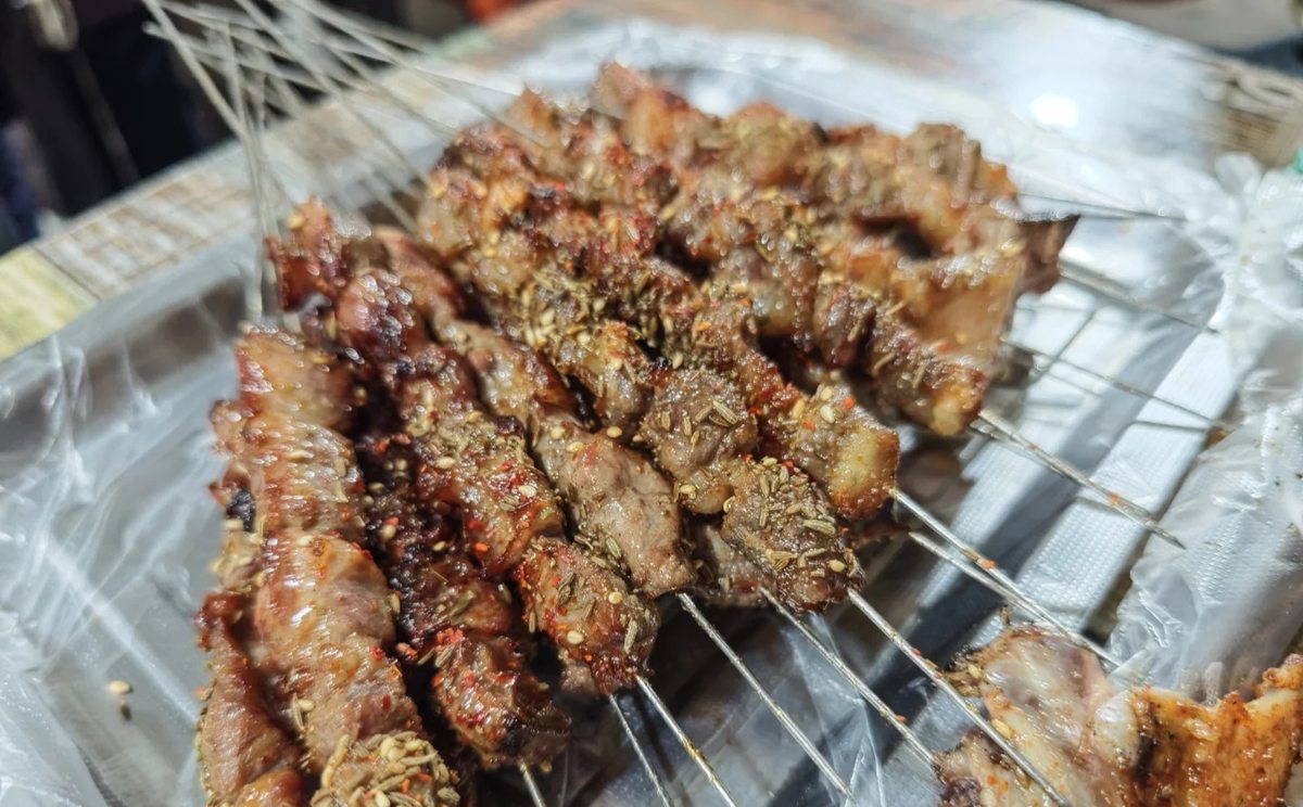 Lamb skewers close-up — the cumin and chilli dusting on the charred, fatty edge