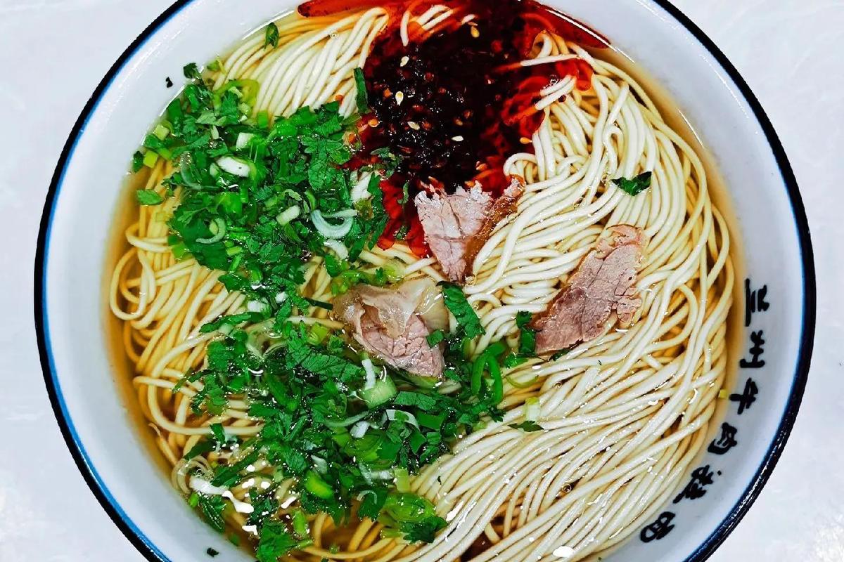 Lanzhou Beef Noodles — a steaming bowl of hand-pulled noodles in clear beef broth with chili oil, sliced radish, and cilantro