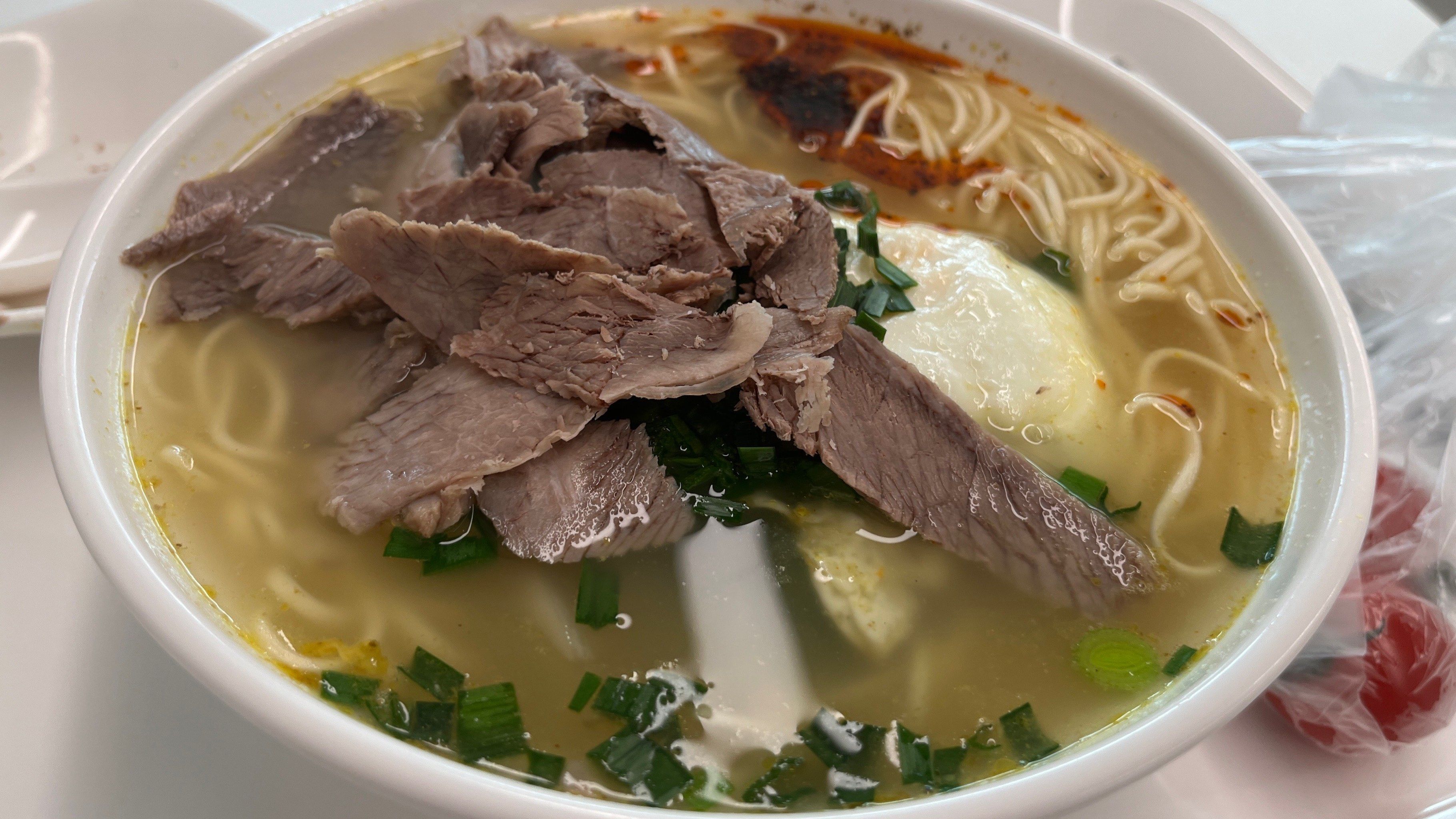 Lanzhou Beef Noodles close-up — hand-pulled noodles glistening with chili oil, sliced beef, and fresh herbs