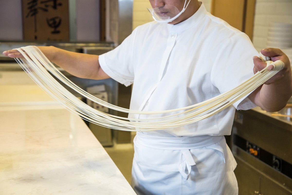 Lanzhou Beef Noodles — a master pulling dough into thin strands in a traditional shop