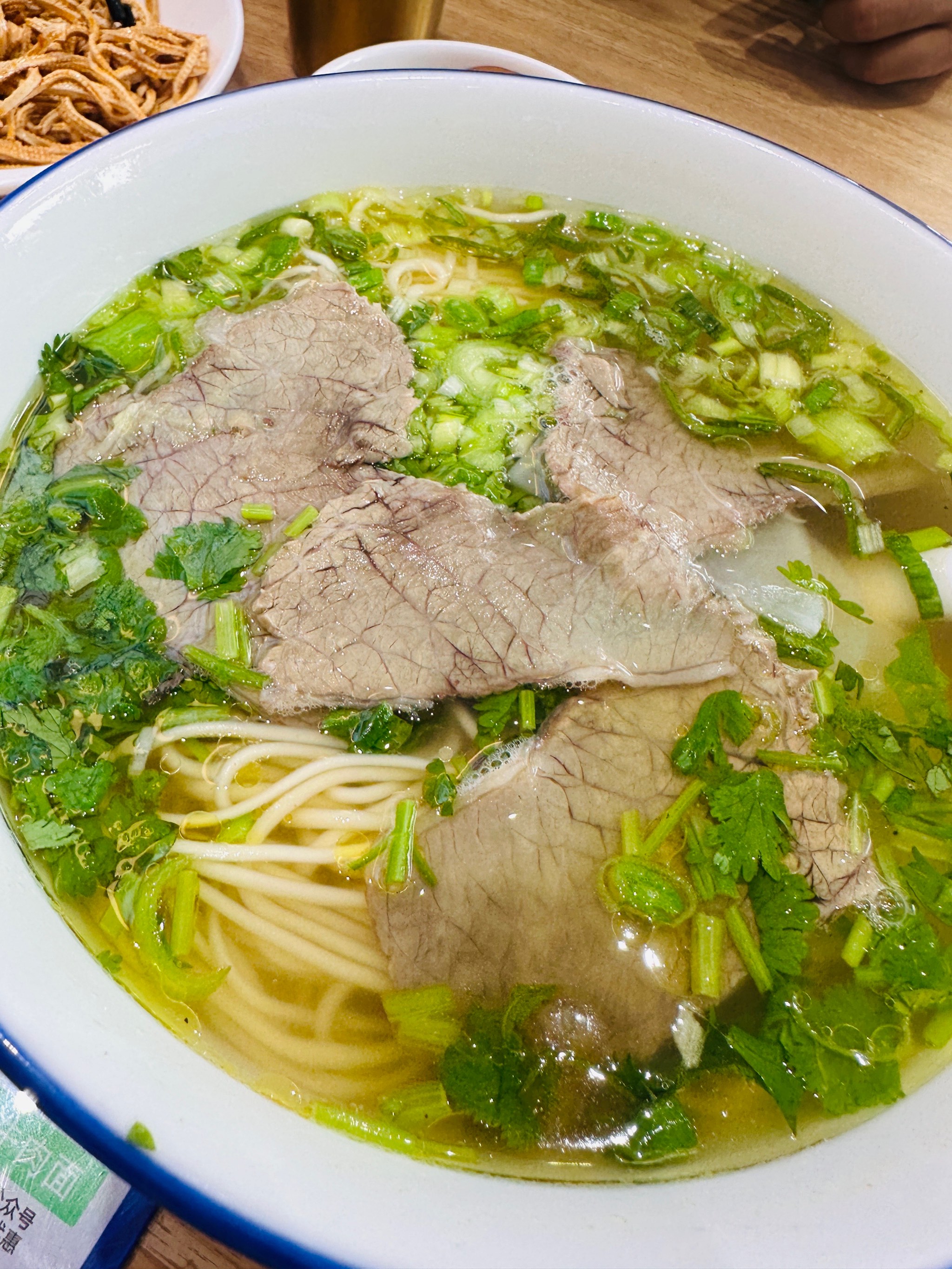 Lanzhou Beef Noodles — the bowl as served, chopsticks lifting a tangle of noodles through chili oil