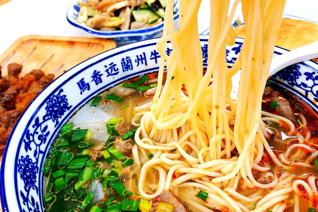 Lanzhou Beef Noodles — the bowl as served, chopsticks lifting a tangle of noodles through chili oil