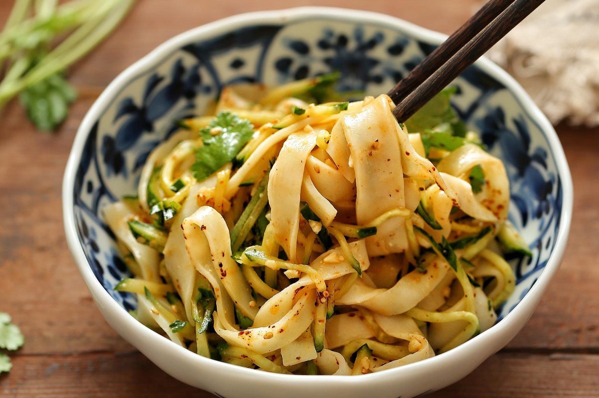 Liangpi — cold, translucent wheat-starch ribbons in a blue-and-white bowl, lifted with chopsticks and slick with chile oil
