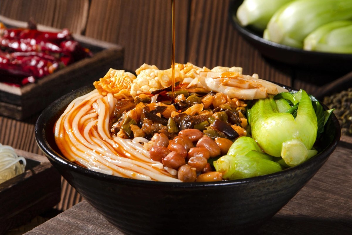 Luosifen — rice noodles in a red snail broth with fried yuba, bamboo shoot and peanuts, chilli oil going in