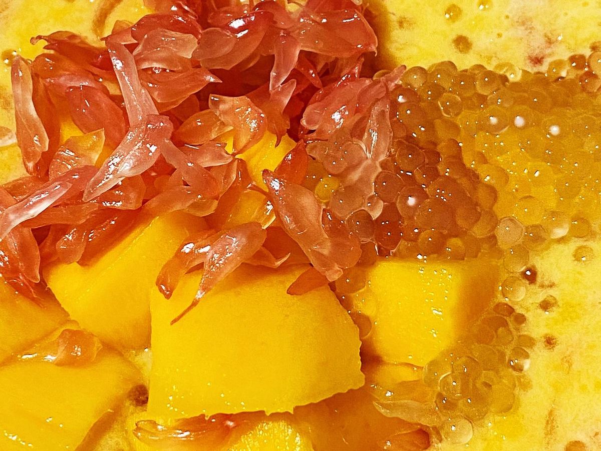 Close-up of mango pomelo sago: translucent sago pearls and pomelo sacs packed into thick mango cream, one spoonful lifted out of the bowl