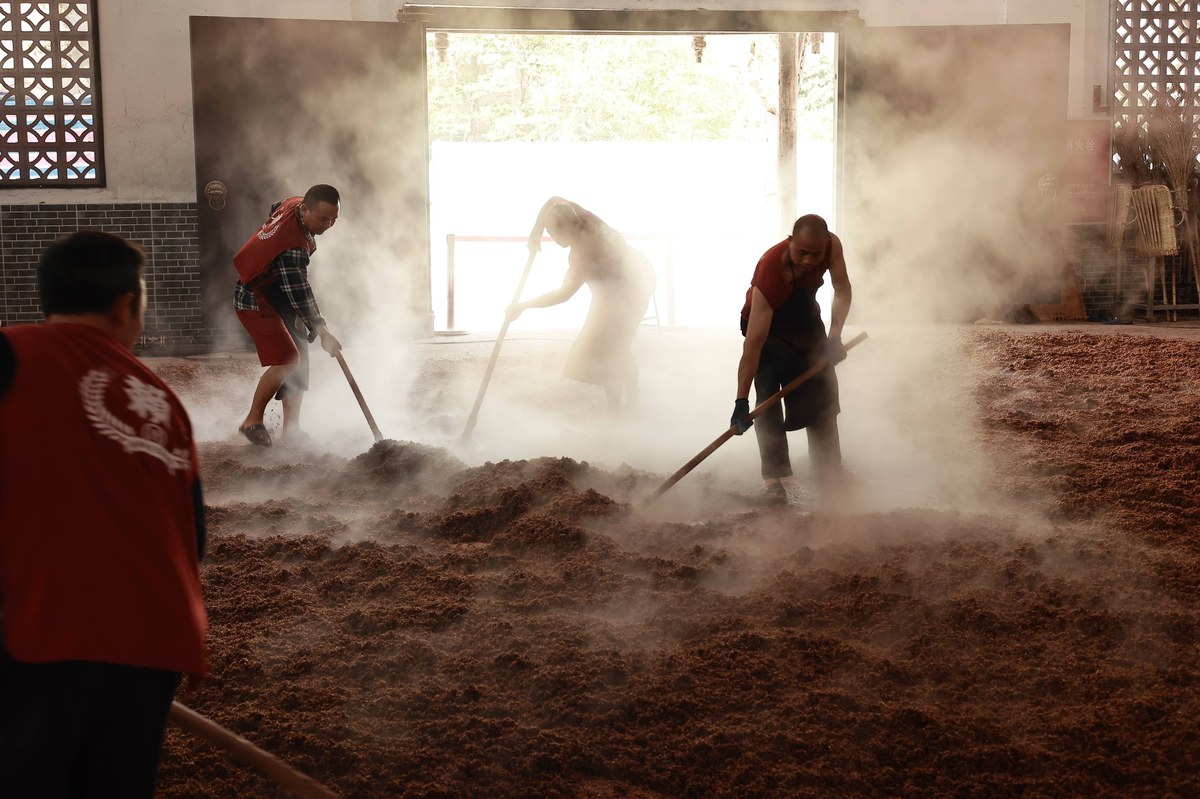 Turning steamed grain by hand in an open-windowed distillery workshop — no sterilisation, just air