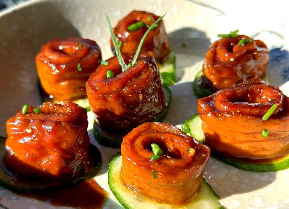 Nine-Turn Intestine close-up — thick glazed rings resting on cucumber slices, the dark sauce pooling around them