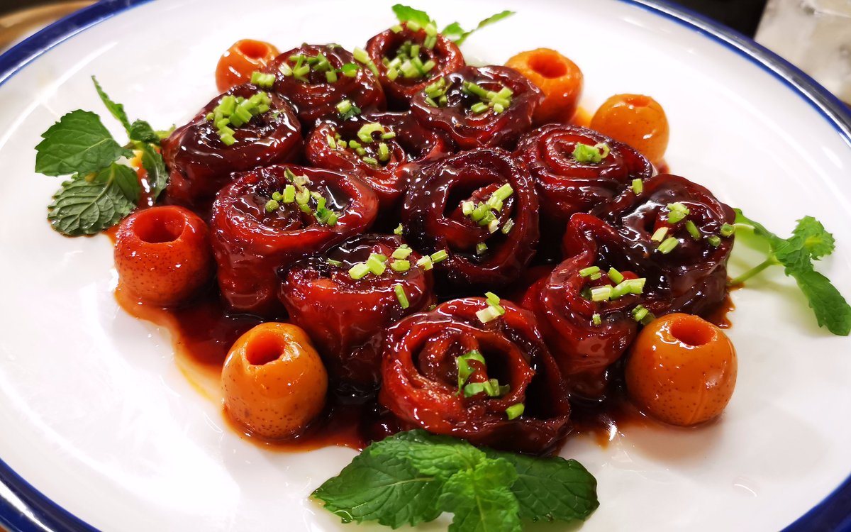 Nine-Turn Intestine served at a restaurant table — glazed rings on a blue-rimmed white plate with fresh herb garnish