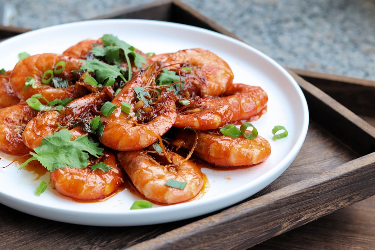 Oil-braised prawns close up — shells coated in a thick red sauce, cilantro and scallion scattered on top