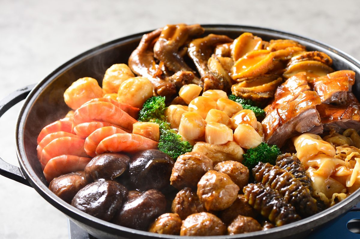 A poon choi basin sitting on a portable burner, still bubbling — one basin, a flame under it, everyone working down through the layers