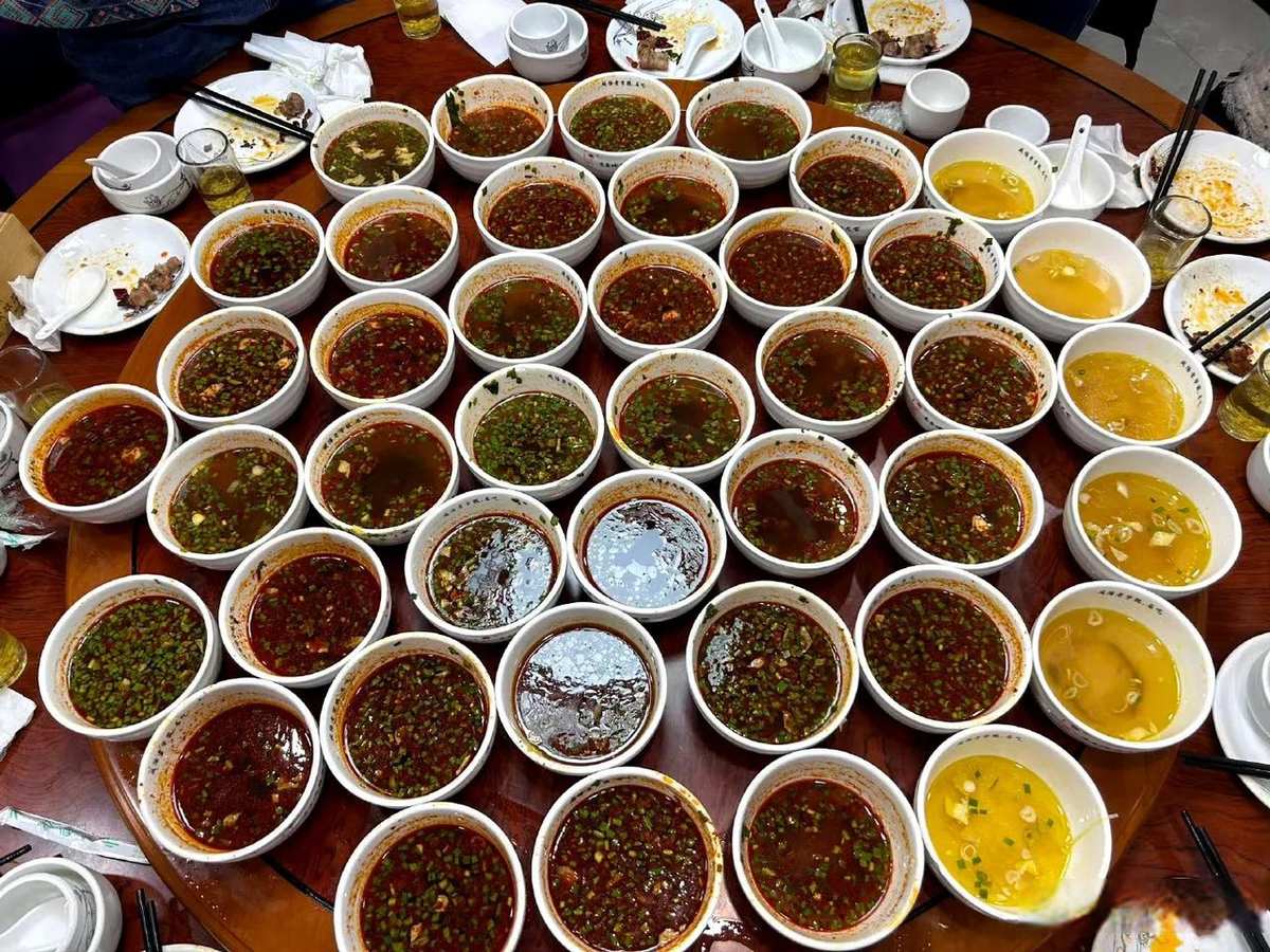 Qishan Saozi Noodles — a banquet table covered end to end with small bowls of red chili-oil broth, the one-mouth serving style the locals call yikouxiang