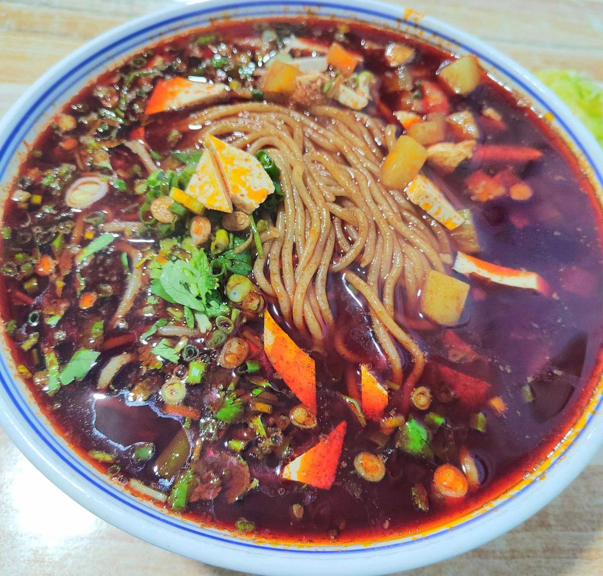 Qishan Saozi Noodles — thin noodles in dark red chili oil with diced carrot, minced pork and chopped scallions, served in a blue-rimmed bowl