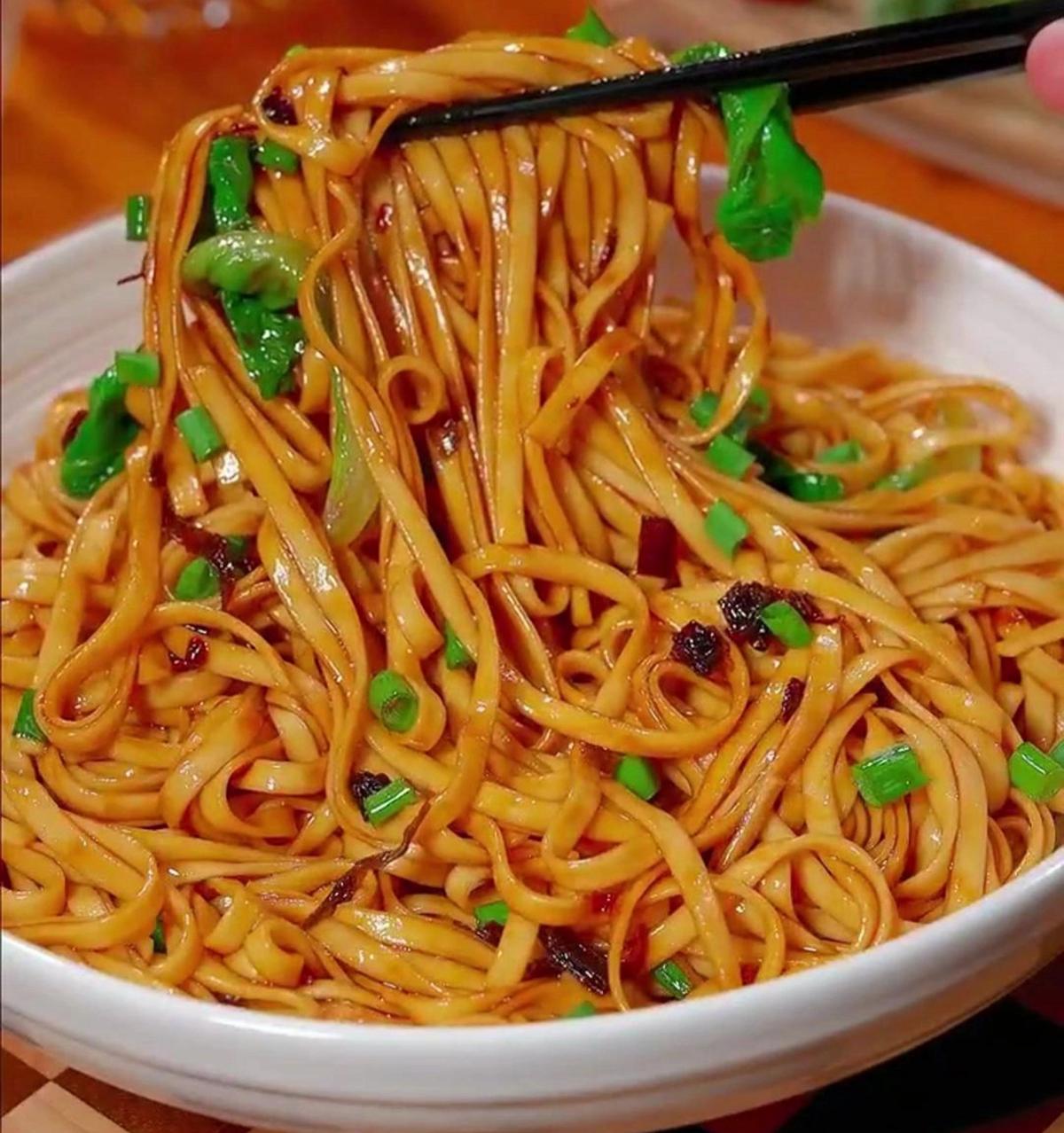 A bowl of scallion oil noodles on a blue-and-white porcelain plate, chopsticks resting beside it, ready to eat