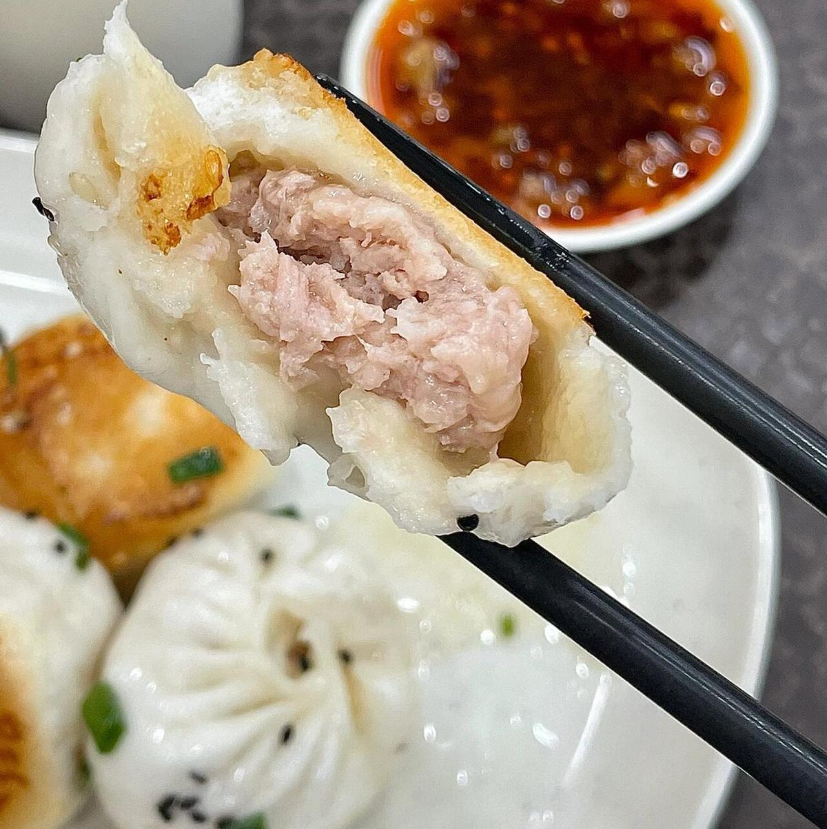 Shengjianbao close-up — golden crispy bottom, sesame seeds, chopped scallions, tear in the dough revealing pork filling